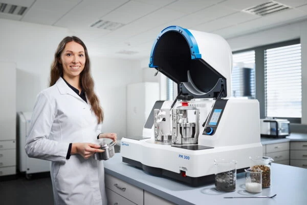 An operator handling a grinding jar beside a laboratory planetary ball mill